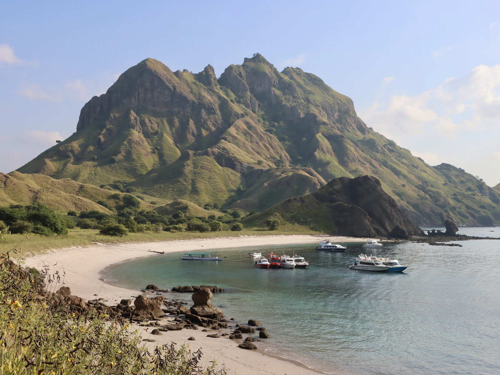 Tour boats in the water near the beach and hills of Komodo National Park