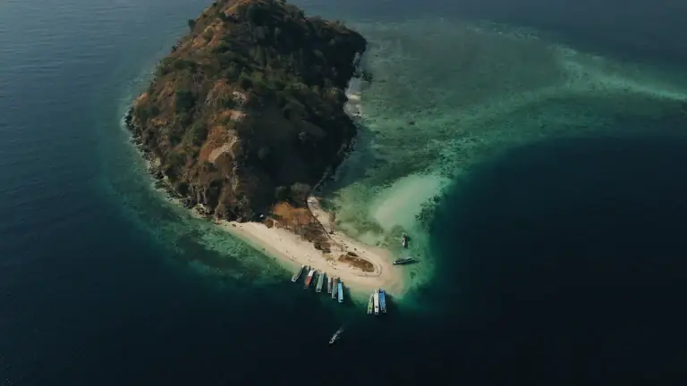 Aerial view of a small island with a sandbar and moored boats in the waters off Labuan Bajo