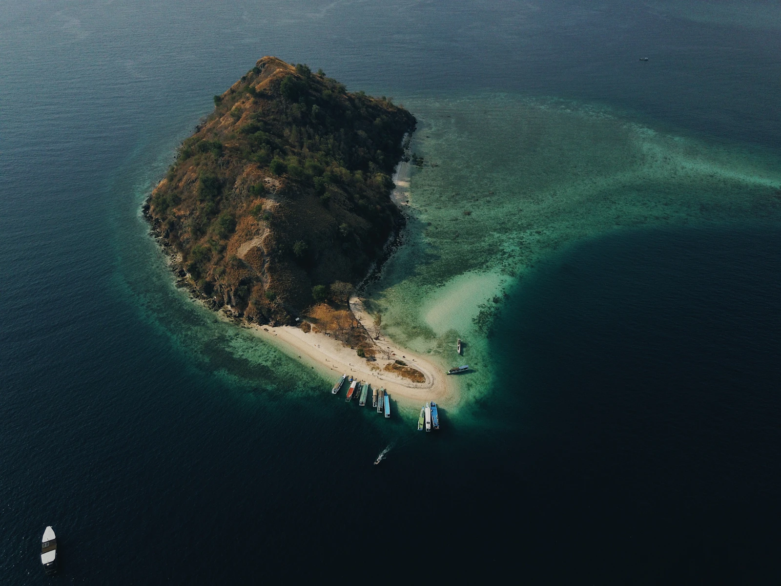 Aerial view of a small island with a sandbar and moored boats in the waters off Labuan Bajo