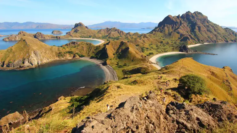 Padar Island's hills and bays seen from the rocky viewpoint at the top of the hiking trail, with hikers on the path below