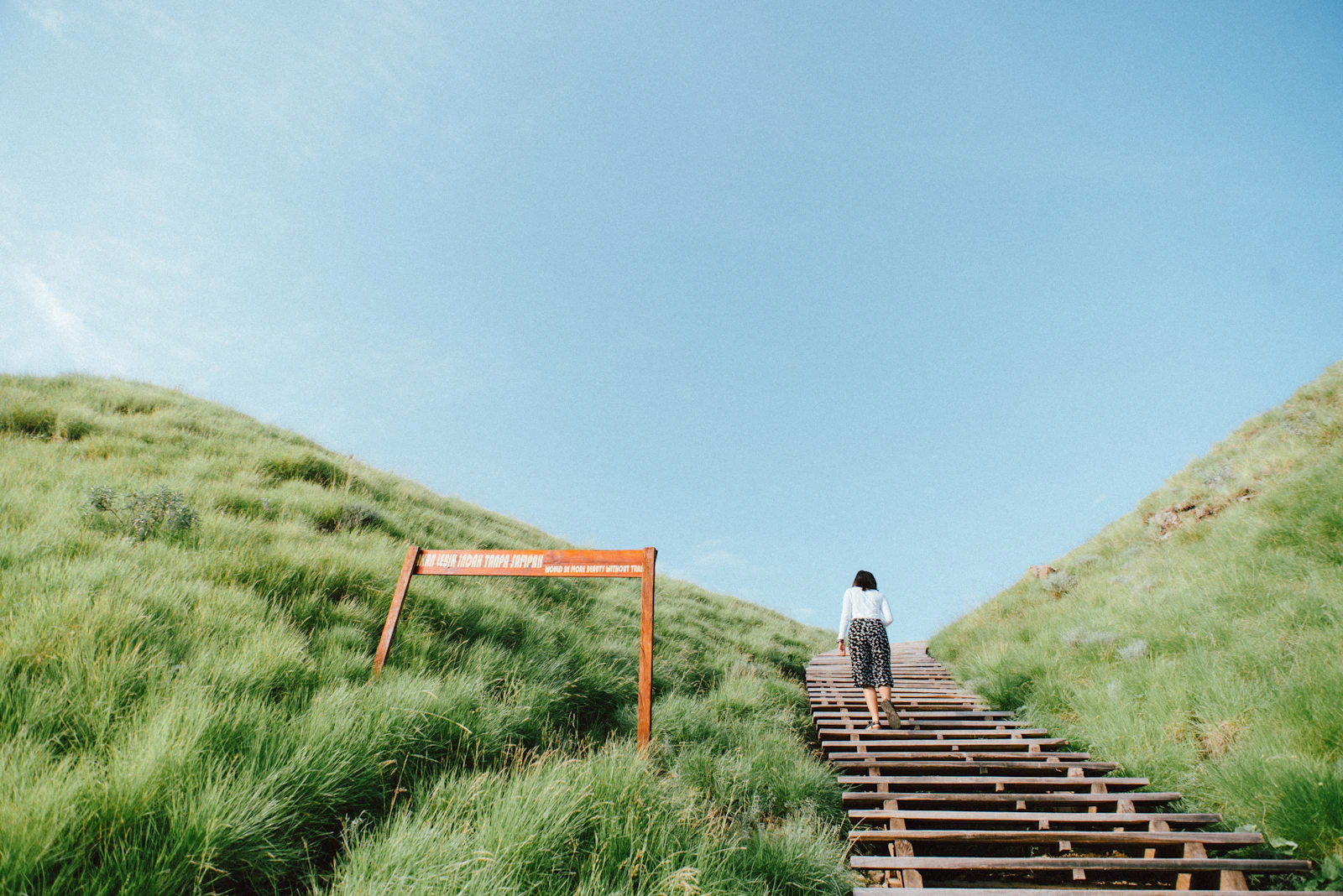 Visitors climbing the wooden stairs of the Padar Island hiking trail surrounded by hillside grass