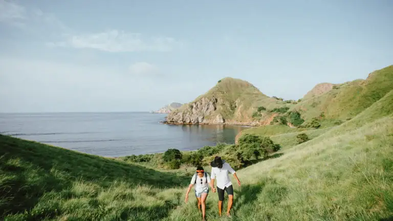 A couple walking along a hillside trail on Padar Island