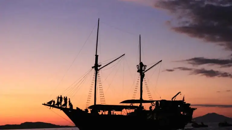 Traditional wooden phinisi sailing boat silhouetted against the sunset sky in the Komodo region