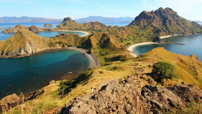 Padar Island's volcanic ridgelines and savanna hills with hikers on the summit trail, seen from the rocky viewpoint at the top