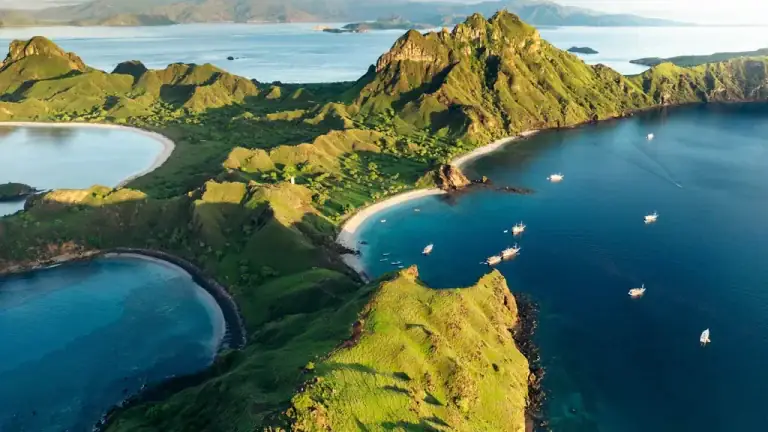 Aerial view over Padar Island's ridges and curved bays in Komodo National Park, with boats anchored offshore