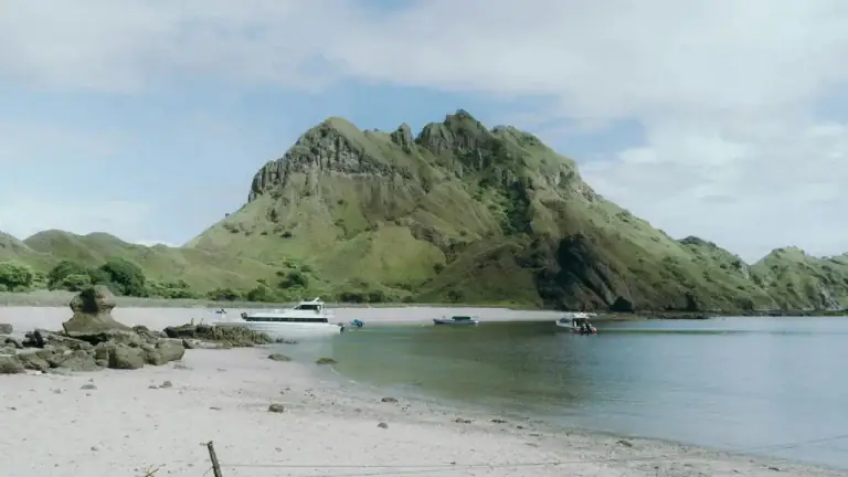 White sand beach on Padar Island with tour boats anchored offshore and a mountain backdrop