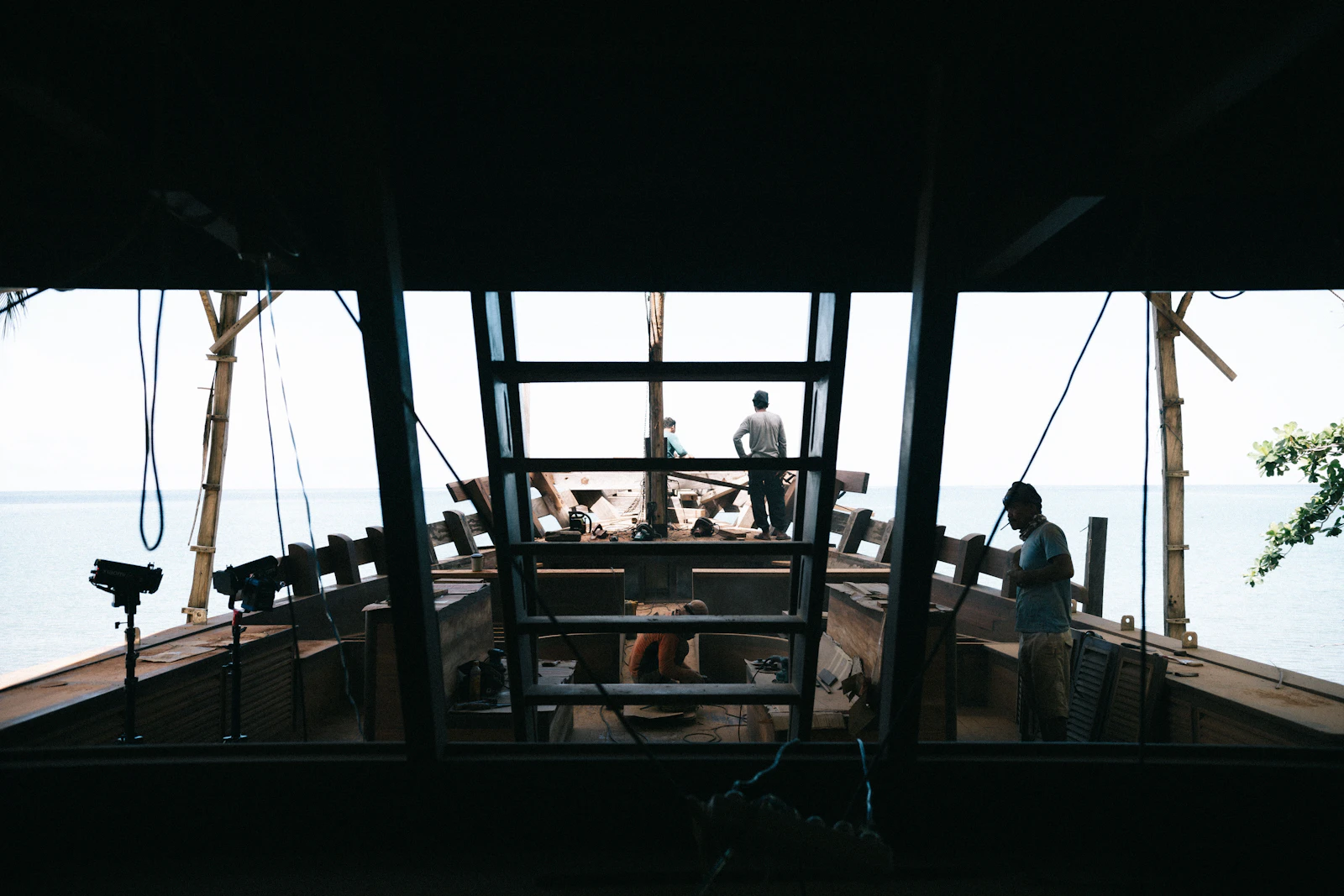 Craftsmen building a traditional wooden phinisi boat at a shipyard workshop