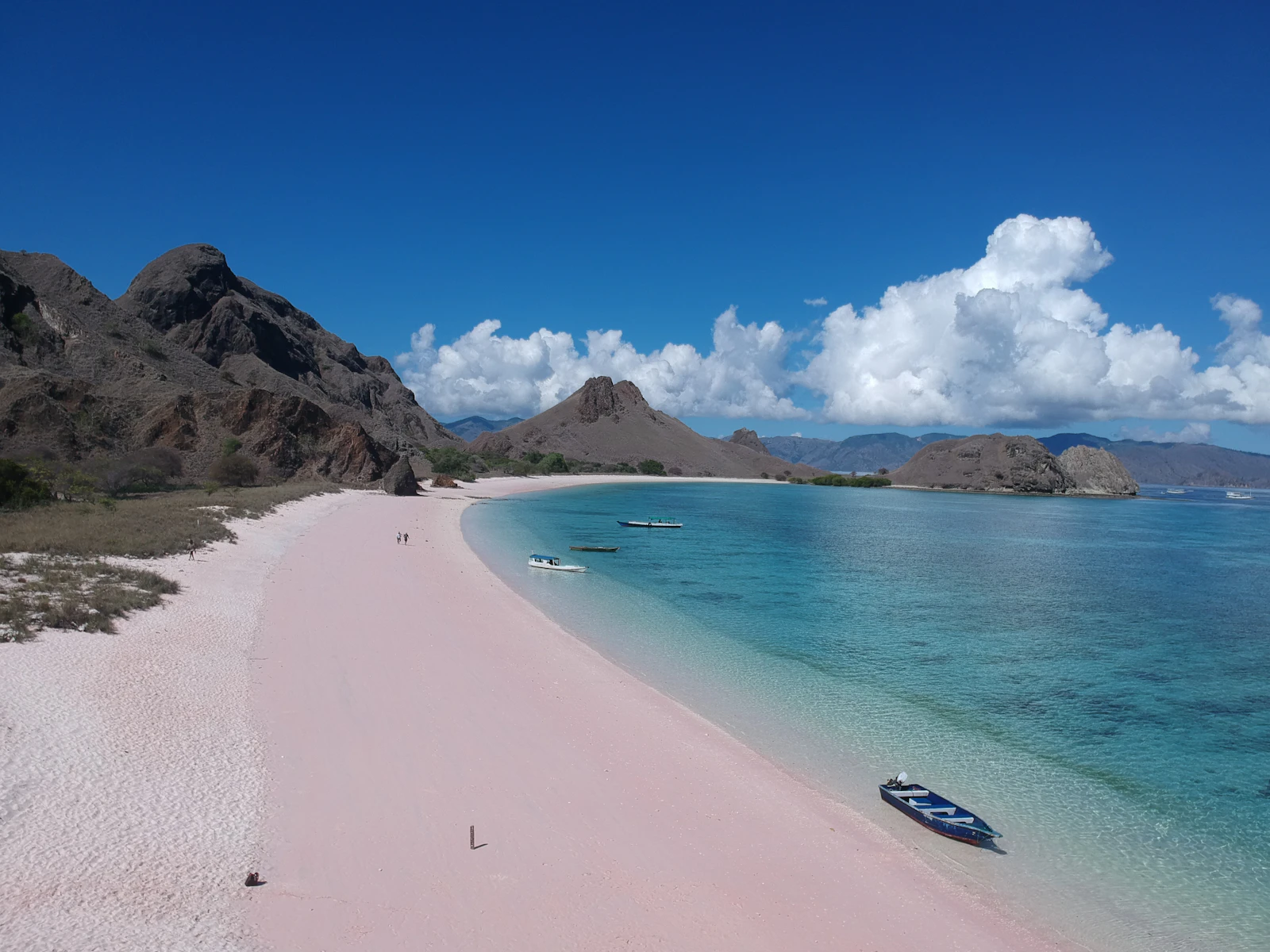 A rose-tinted sand beach with clear water and hills in the background